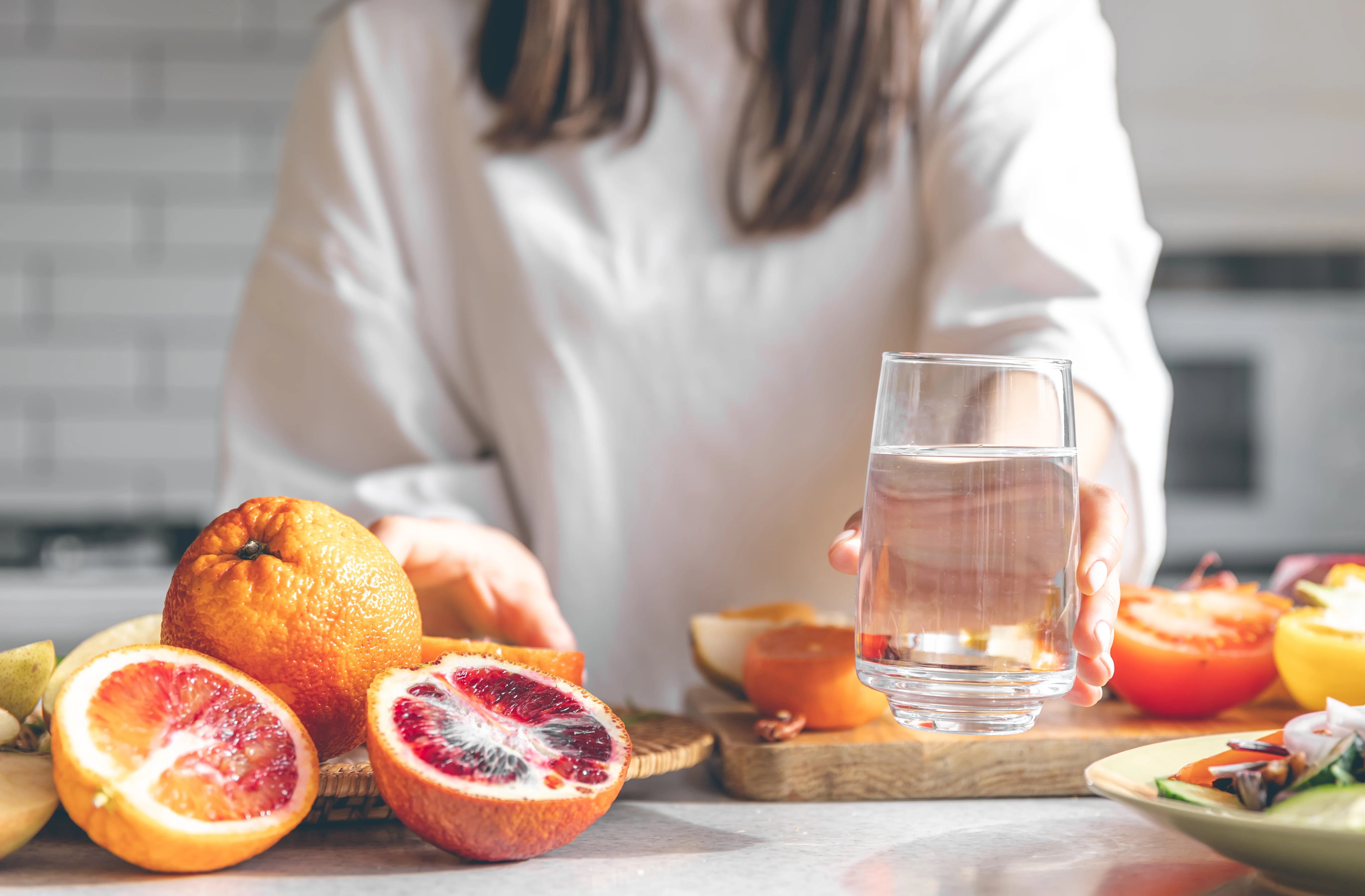Woman holding a clear glass of water in a kitchen with fresh fruit