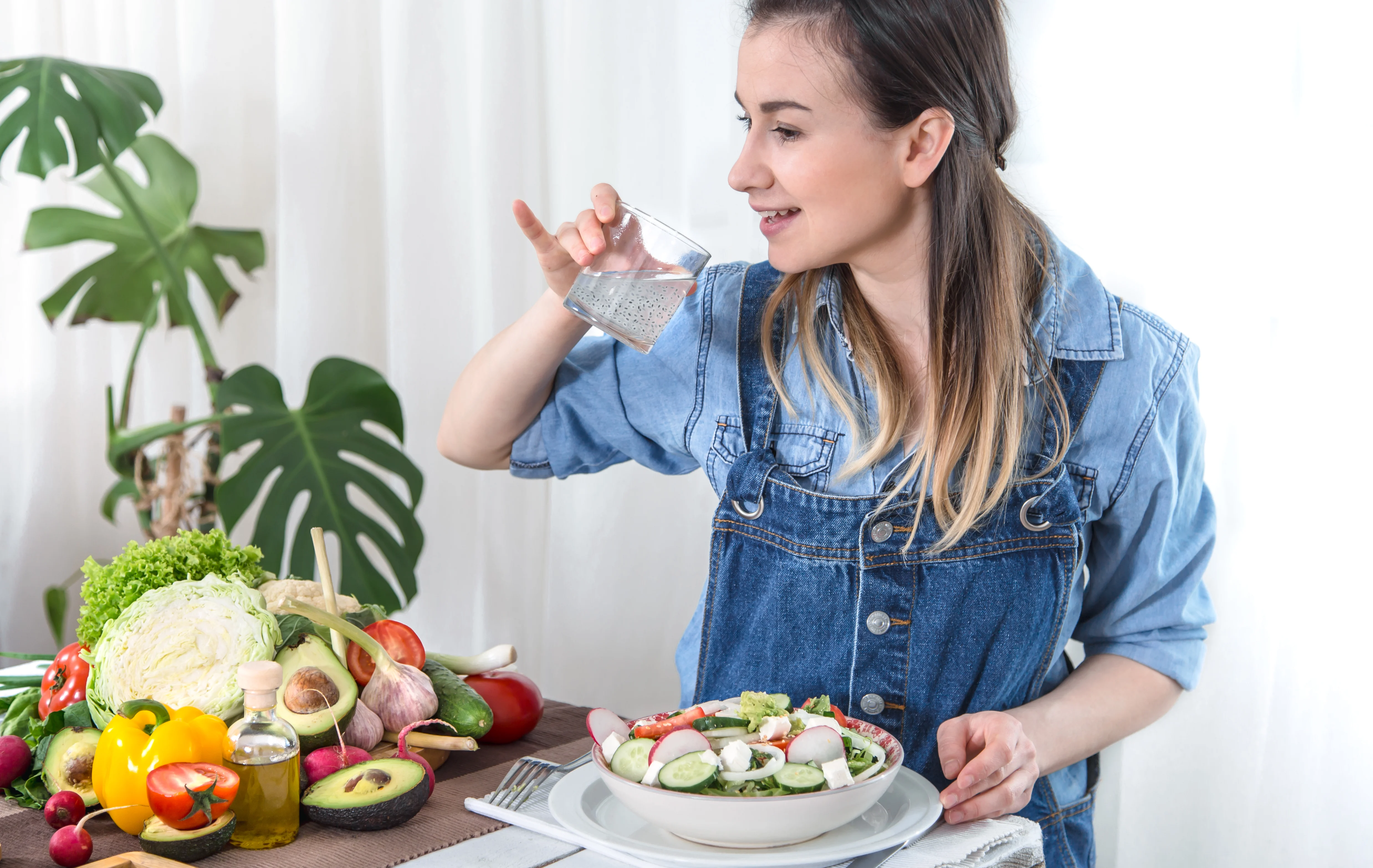 Woman drinking water alongside a fresh vegetable meal